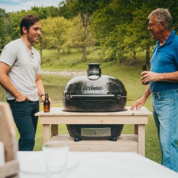 Charcoal Primo Grill with two men drinking beer and talking as the food cooks in the grill