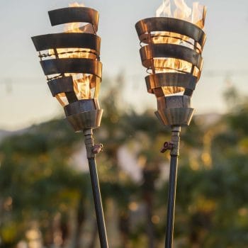 The Outdoor Plus Spiral Fire Torch is a handcrafted lighting fixture made in the USA, designed to serve as both functional art and a premium flame feature for patios, pool areas, or landscapes. Constructed from high-grade 304 stainless steel, it is built to withstand extreme temperatures and natural elements while resisting rust and corrosion. This modern torch operates at a maximum heat output of 20,000 BTU/hr and is compatible with either natural gas or liquid propane. It utilizes a simple match-lit ignition system and is available with two base options: the "Original TOP" base, which features a needle valve for precise flame adjustment and fits standard 2.5-inch posts, and the "TOP-LITE" base, designed for quick installation onto any 0.5-inch gas pipe.